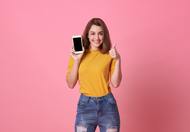 Portrait of happy young woman showing at blank screen mobile phone isolated over pink background. - Foto, Imagen