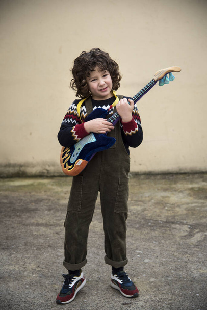 menino tocando e experimentando com uma guitarra de brinquedo com cores marcantes
 - Foto, Imagem