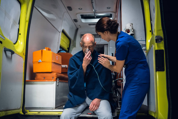 Doctor in uniform staat met de man die zit in zuurstofmasker in deken - Foto, afbeelding