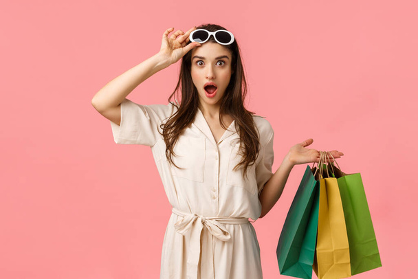 Chodźmy na zakupy. Zabawiona i podekscytowana kobieta zakupy dobrze się bawiąc przeglądając centra handlowe, trzymając torby sklepowe, zdejmując okulary widząc dokładnie to, czego szukaliśmy, różowe tło - Zdjęcie, obraz