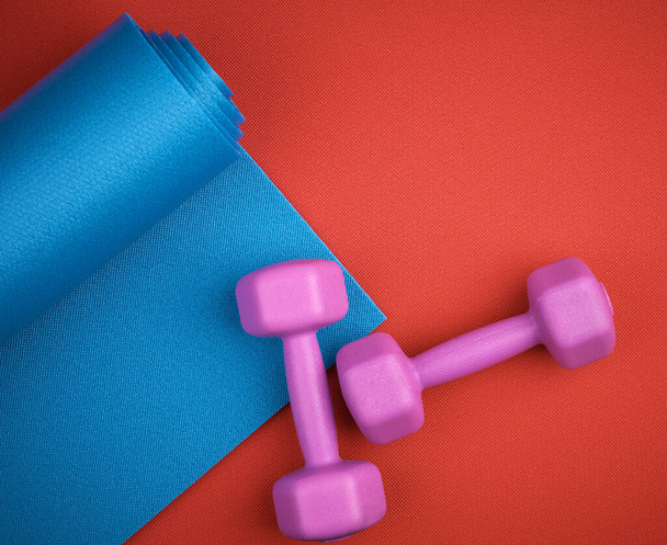пара фіолетових пластикових гантелів і синій неопреновий килимок
 - Фото, зображення