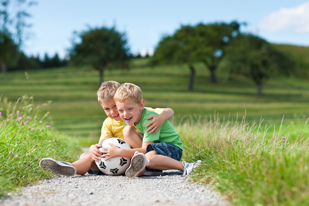 duas crianças com futebol sentado em uma estrada de terra
 - Foto, Imagem