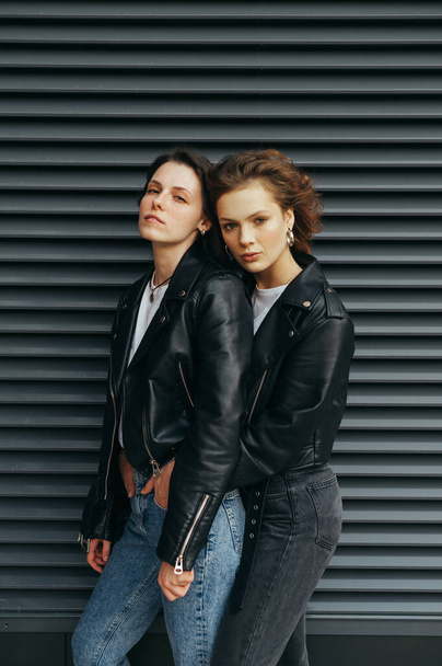 Fashion portrait of two stylish girls standing against a black w - Foto, imagen