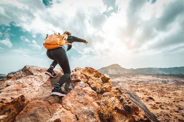 Женщина-туристка с рюкзаком поднимается на гору, указывая на небо
 - Фото, изображение