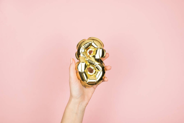 Gold foil balloons numeral 8 in femine hand on pink background. Happy Womens Day - Φωτογραφία, εικόνα