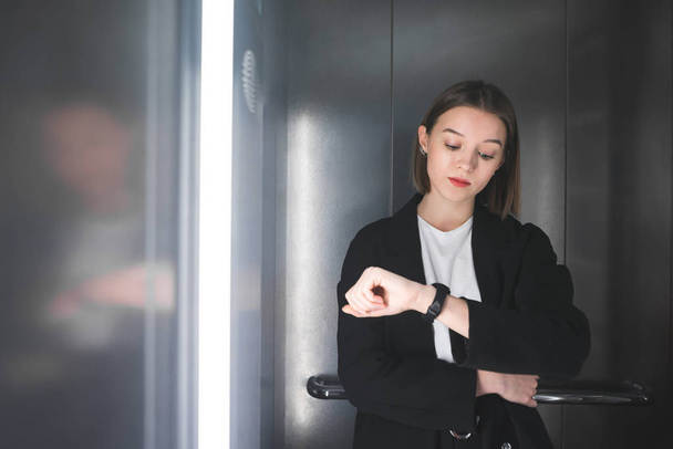 İşçisi kadın ofis bekleyen asansörde yoruldu. Genç işçi saati asansörde bekleyen sıkılmış bakıyor. - Fotoğraf, Görsel