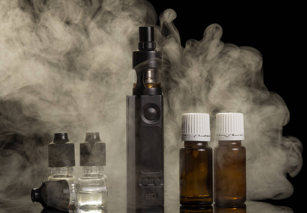 Cloud of steam from an electronic cigarette, bottles of liquid for smoking, isolated on black - Foto, Imagem