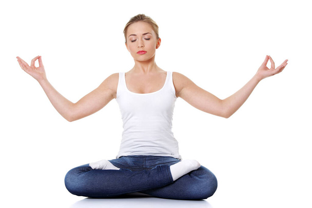 Portrait of young pretty student girl over white background meditating in lotus pose. She is relaxed and concentrated - Photo, image