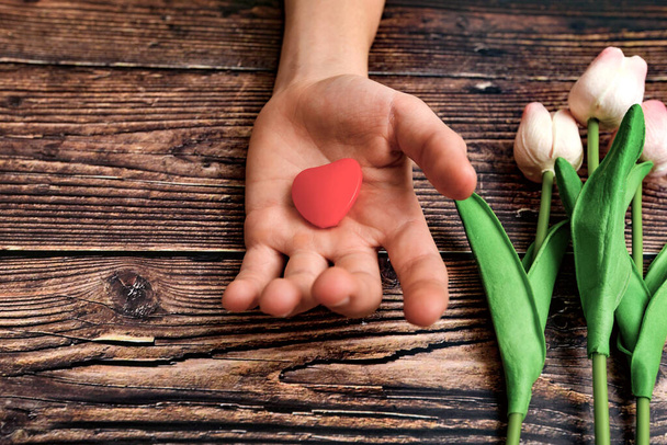 Man offers a heart and tulips on a brown wooden background. The concept of the holiday of Valentine's Day, and International Women's Day March 8. - Foto, Bild