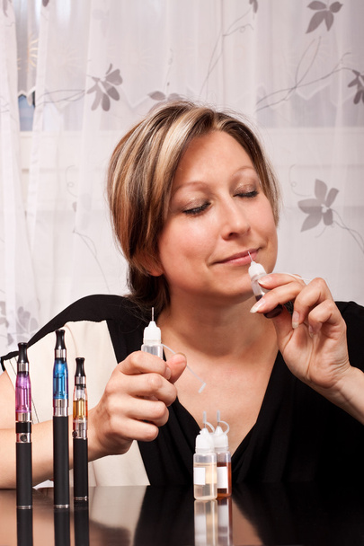 Blonde young woman smelling liquid for e cigarette - Photo, Image