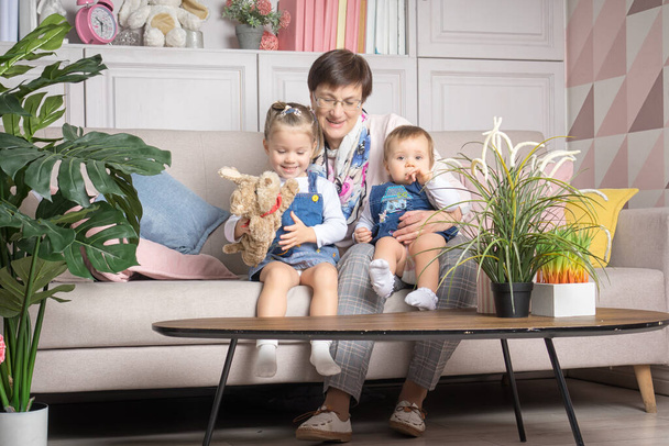 Großmutter sitzt mit zwei Enkelinnen auf der Couch im Wohnzimmer und zeigt ihnen ein Puppenspiel - Foto, Bild