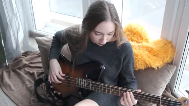 young beautiful girl playing guitar by the window - Materiaali, video