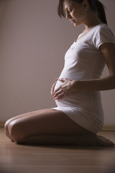 Pregnant woman kneels looking down holding stomach - Photo, Image