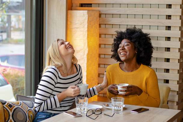 schwarzafrikanische schöne junge Frau, die im Café sitzt, Musik hört oder mit Ohrhörern in den Ohren telefoniert und eine Tasse Kaffee genießt. - Foto, Bild