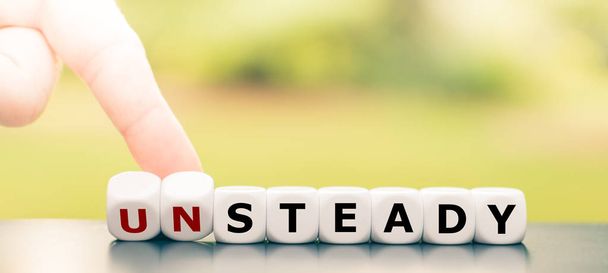 Hand turns dice and changes the word "unsteady" to "steady". - Photo, Image