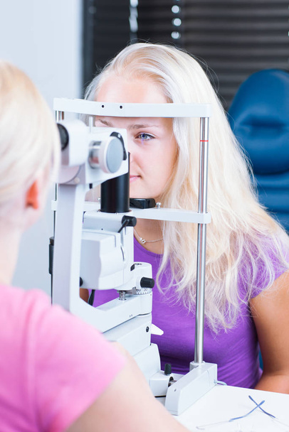 optometry concept - pretty, young female patient having her eyes examined by an eye doctor (color toned image - Foto, imagen