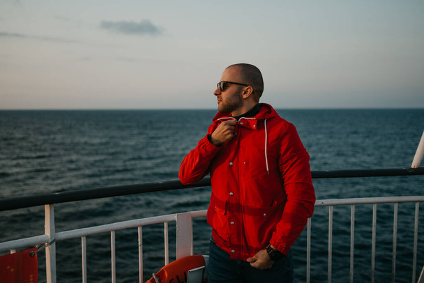 夕日を見ながら船に乗って彼の赤いジャケットを固定します。. - 写真・画像