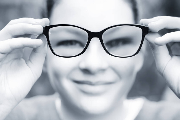 Miyop gözlüklü genç kız. Kız gözlüğünü kameranın önünde iki eliyle tutuyor - gözlüğe odaklan - alanın sığ derinliği - Fotoğraf, Görsel
