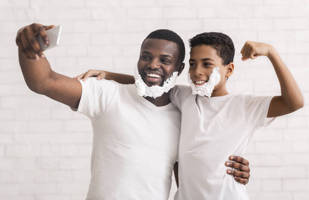 Selfie masculin. Papa et fils s'amusent ensemble, posant avec de la mousse à raser sur la caméra du téléphone portable, fond de studio gris
 - Photo, image