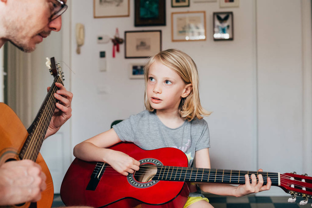 vader leren zijn dochter hoe om gitaar te spelen - Foto, afbeelding