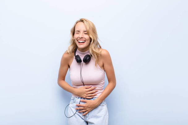 young blonde woman laughing out loud at some hilarious joke, feeling happy and cheerful, having fun listening music - Fotó, kép