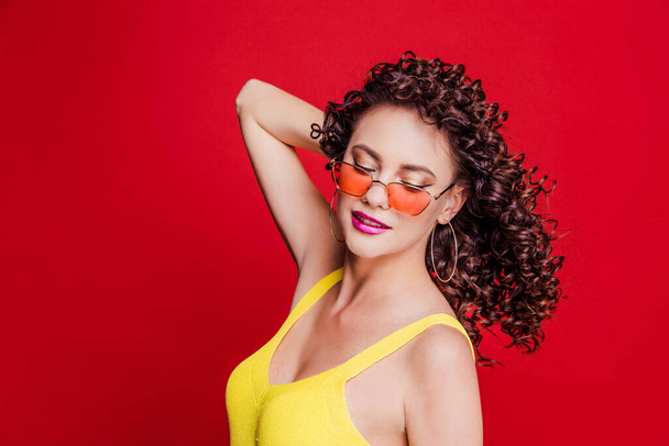 Beautiful happy brunette girl with curly hair and a yellow t-shirt posing on a red background - Fotoğraf, Görsel