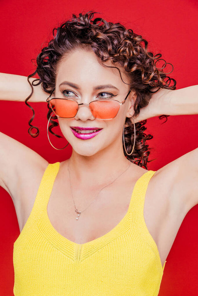 Beautiful happy brunette girl with curly hair and a yellow t-shirt posing on a red background - Photo, Image