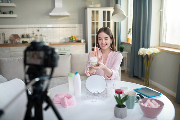 Cute young girl in a pink shirt explaining online how to use new cream - Foto, Bild