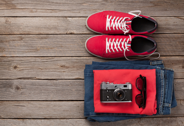 Ρούχα και αξεσουάρ. Sneakers, τζιν και κάμερα. Αστική ενδυμασία για καθημερινές ή ταξιδιωτικές διακοπές σε ξύλινο φόντο με χώρο αντιγραφής. Πάνω όψη επίπεδη lay - Φωτογραφία, εικόνα