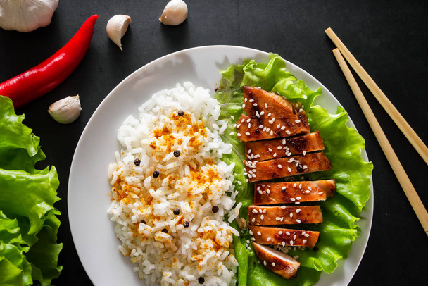 Kurczak Teriyaki z białym ryżem na talerzu. Smaczne jedzenie i chińskie paluszki na ciemnym tle - Zdjęcie, obraz
