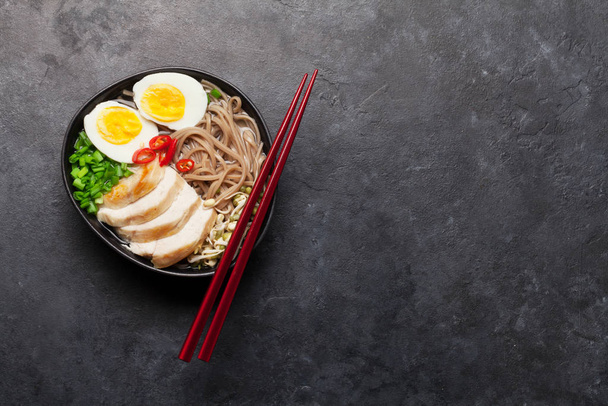 Sopa de ramen de fideos asiáticos con pollo, verduras y huevos sobre fondo de piedra. Vista superior plano con espacio de copia
 - Foto, Imagen