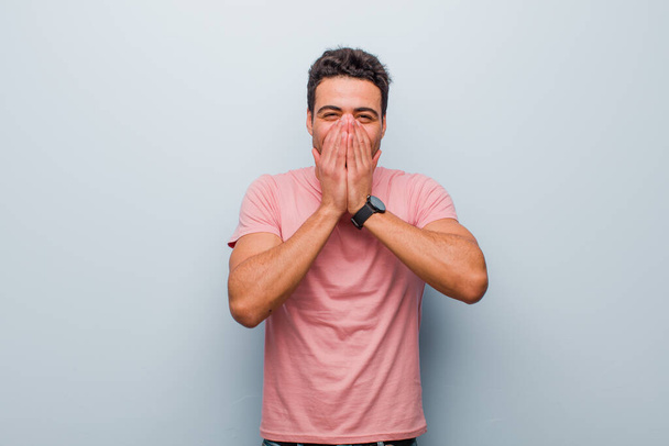 young arabian man looking happy, cheerful, lucky and surprised covering mouth with both hands against gray wall - Photo, image