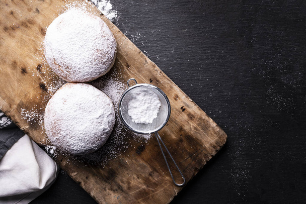 Top view of two donuts covered with powdered sugar on the wooden cutting board and stony worktop. - Фото, зображення