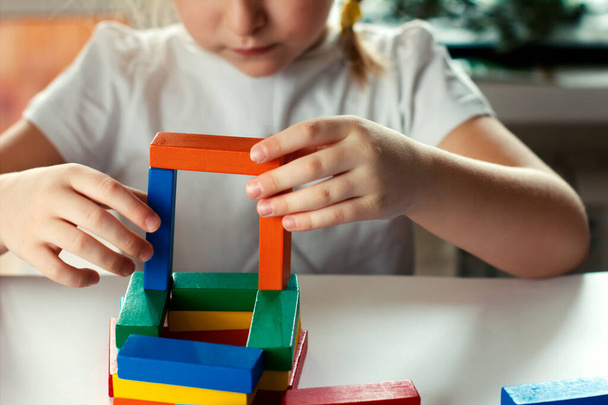 Petite fille blonde jouant à des jeux de société. blocs de construction en bois dans les mains de la fille
. - Photo, image