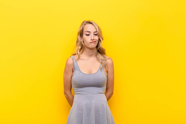 young blonde woman looking goofy and funny with a silly cross-eyed expression, joking and fooling around against orange wall - Photo, image