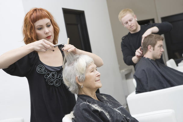 Stylist cuts elderly woman's hair - Zdjęcie, obraz