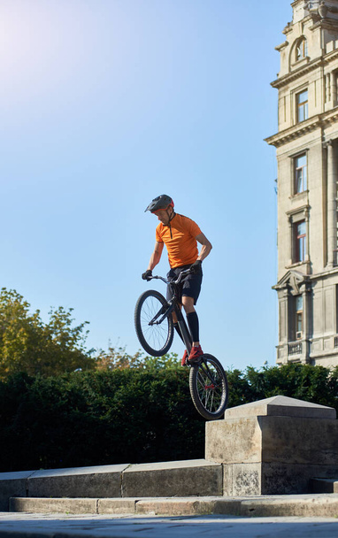 Trial biker staat op het achterwiel van zijn mountainbike op een prachtige zonnige dag boven de blauwe lucht, concept van actieve levensstijl - Foto, afbeelding