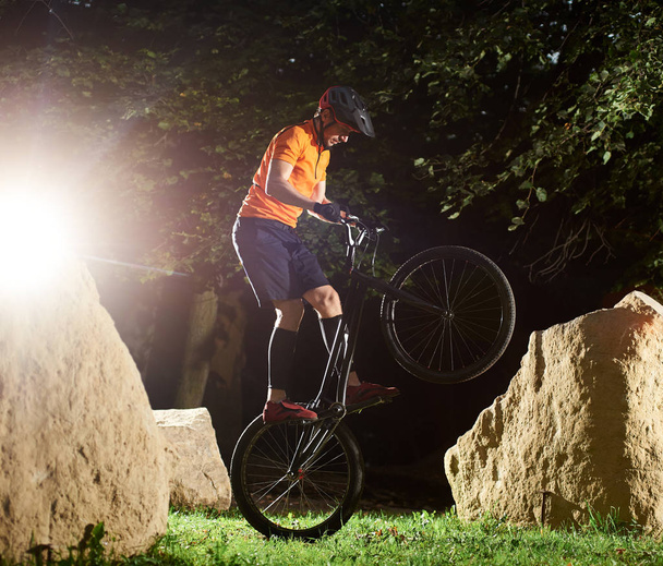 Cycliste extrême sur bmx vélo dans le parc effectuant cascade en gardant l'équilibre sur la roue arrière, vue latérale
 - Photo, image