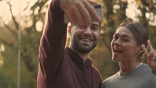 Крупним планом Радісна молода красива пара робить селфі на смартфоні в парку на відкритому повітрі
 - Кадри, відео