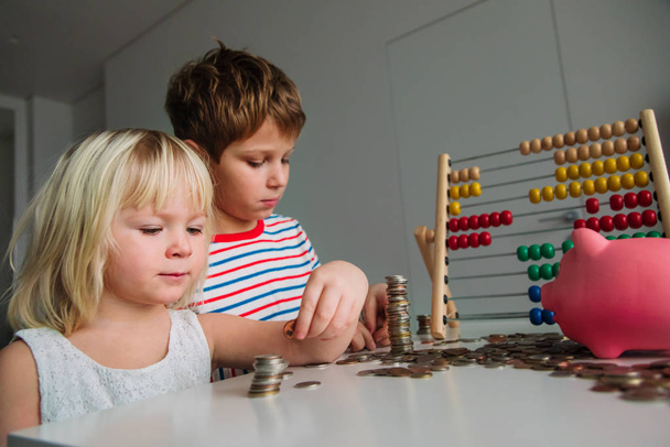 kids count and save money, girl and boy put coins into piggy bank - Fotó, kép
