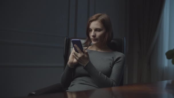 Young businesswoman working in business office at night. Woman surfing online in smartphone sitting in cozy office leather armchair.  - Footage, Video