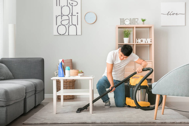 Young Asian man hoovering floor at home - Foto, Bild