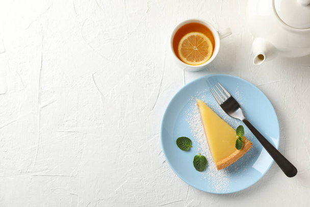 Talíř s plátkem citronového koláče, konvicí a šálkem čaje na bílém hřbetě - Fotografie, Obrázek