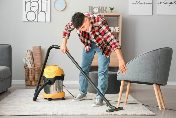 Young Asian man hoovering floor at home - Foto, afbeelding