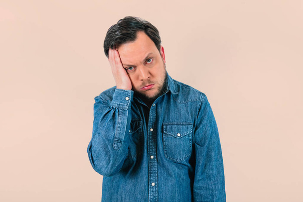 Young man with expression of extreme tiredness and sadness. Denim shirt and isolated white background. - Photo, Image