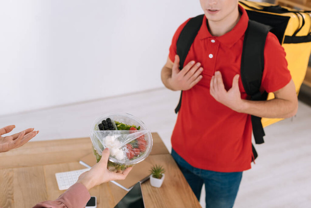Cropped view of businesswoman with takeaway salad near confused courier  - Photo, Image
