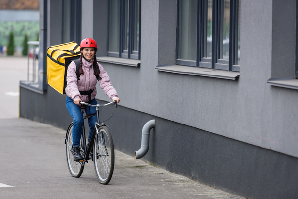 Courrier souriant avec sac à dos thermo équitation vélo près du bâtiment
 - Photo, image