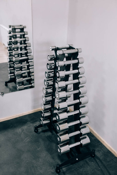 Conjunto de halteres negros. Feche muitos halteres de metal no rack no centro de fitness esportivo, conceito de equipamento de treinamento de peso
. - Foto, Imagem