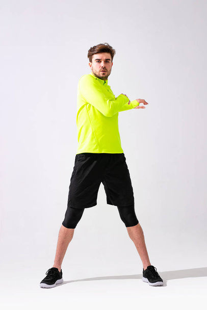 doing stretching first. young man in sportwear training and stretching his muscle on white background - Foto, Bild