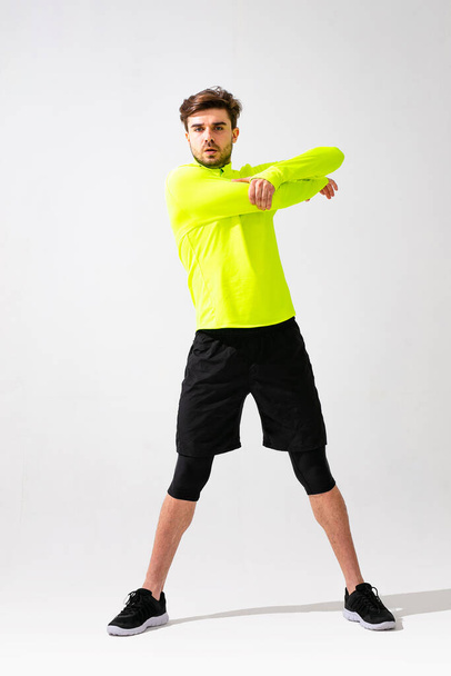 doing stretching first. young man in sportwear training and stretching his muscle on white background - Fotografie, Obrázek
